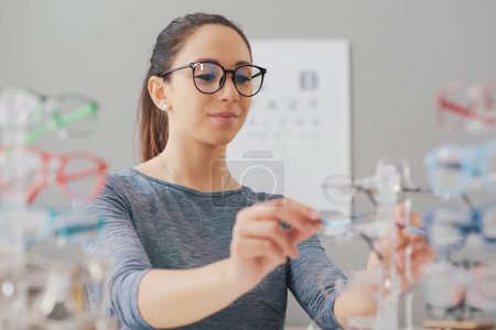 Téléchargez les photos : Jeune femme heureuse chez l'opticien, elle achète de nouvelles lunettes de vue - en image libre de droit
