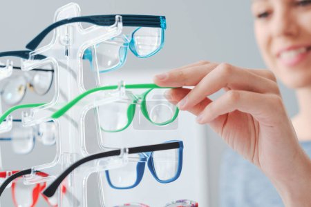 Téléchargez les photos : Joyeux jeune femme au magasin d'optique, elle choisit de nouvelles lunettes élégantes, concept de soins oculaires - en image libre de droit