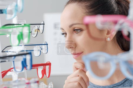 Téléchargez les photos : Joyeux jeune femme au magasin d'optique, elle choisit de nouvelles lunettes élégantes, concept de soins oculaires - en image libre de droit