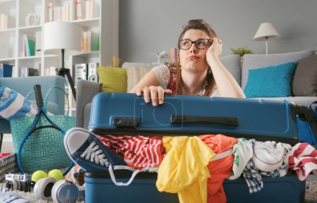 Photo for Tired sad woman packing for a long journey, she is leaning on her overpacked trolley bag: travel, vacations and tourism concept - Royalty Free Image