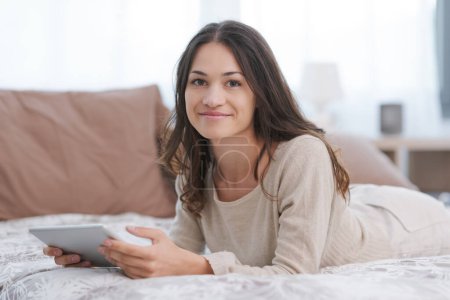 Téléchargez les photos : Happy young woman relaxing at home and connecting online with her digital tablet, entertainment and technology concept - en image libre de droit