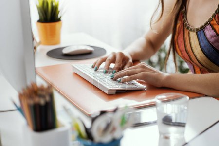 Photo for Woman sitting at desk and typing on a keyboard, she is working from home - Royalty Free Image