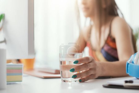 Téléchargez les photos : Femme se connectant avec son ordinateur et l'eau potable - en image libre de droit