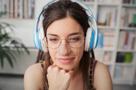 Photo for Young woman sitting at desk at home, she is watching the computer screen and wearing headphones - Royalty Free Image