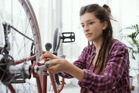 Téléchargez les photos : Femme confiante réparant son propre vélo à la maison, elle utilise une clé à molette et des roues de contrôle - en image libre de droit