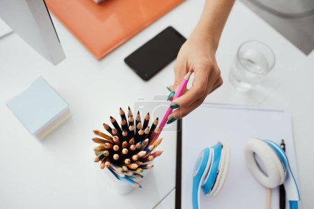 Téléchargez les photos : Jeune designer assise au bureau et travaillant, elle prend un crayon de couleur, la créativité et l'imagination concept - en image libre de droit