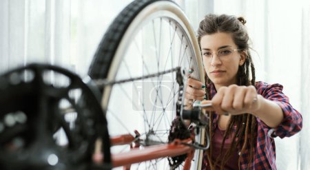 Téléchargez les photos : Femme confiante réparant son propre vélo à la maison, elle utilise une clé à molette et des roues de contrôle - en image libre de droit