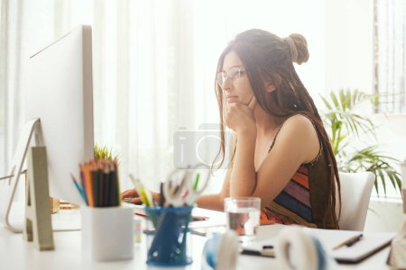 Foto de Mujer creativa joven sentada en el escritorio y trabajando con su computadora - Imagen libre de derechos