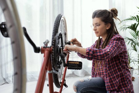 Foto de Joven mujer confiada reparando su bicicleta en casa - Imagen libre de derechos