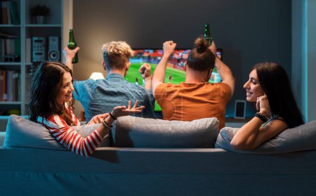 Foto de Chicas aburridas hablando y cotilleando mientras sus novios están viendo fútbol en la televisión - Imagen libre de derechos