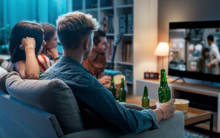 Téléchargez les photos : Groupe d'amis assis sur le canapé à la maison et regardant des films ensemble - en image libre de droit