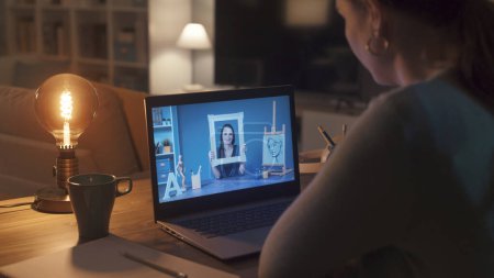 Foto de Mujer conectándose con su portátil y tomando clases de arte en línea, un profesor está mostrando un marco y hablando en un webinar - Imagen libre de derechos