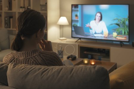 Téléchargez les photos : Femme assise sur le canapé et regardant une nutritionniste parler de régimes à la télévision - en image libre de droit