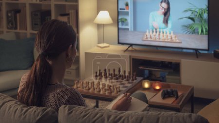 Foto de Mujer sentada en el sofá y aprendiendo a jugar al ajedrez, ella está viendo un programa de televisión - Imagen libre de derechos
