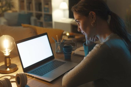 Téléchargez les photos : Jeune femme assise au bureau et connectée à son ordinateur portable à la maison, concept de technologie et de communication - en image libre de droit