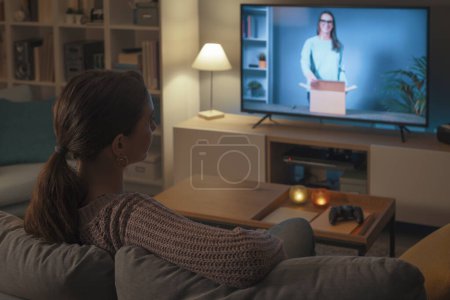Foto de Mujer relajándose en el sofá y viendo un video de unboxing en línea en su smart TV - Imagen libre de derechos