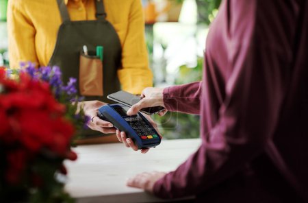 Foto de Cliente pagando en una florería usando su smartphone, concepto de pagos electrónicos - Imagen libre de derechos