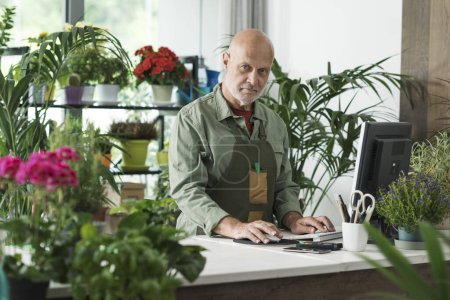 Téléchargez les photos : Fleuriste professionnel travaillant dans son atelier d'usine, il utilise un ordinateur et prend des commandes en ligne - en image libre de droit