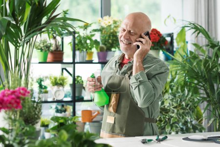 Téléchargez les photos : Fleuriste et jardinier professionnel travaillant dans sa boutique, il reçoit un appel téléphonique - en image libre de droit