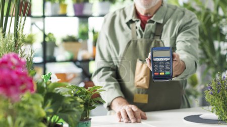 Photo for Business owner in his flower shop, he is holding a POS payment terminal, cashless electronic payments concept - Royalty Free Image