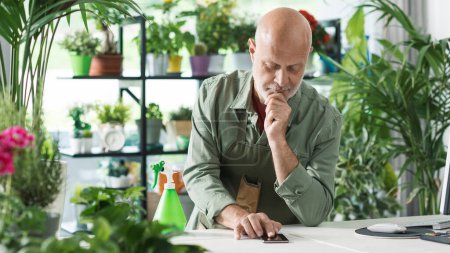 Foto de Florista profesional que trabaja en una tienda de plantas, está recibiendo órdenes en su teléfono inteligente - Imagen libre de derechos