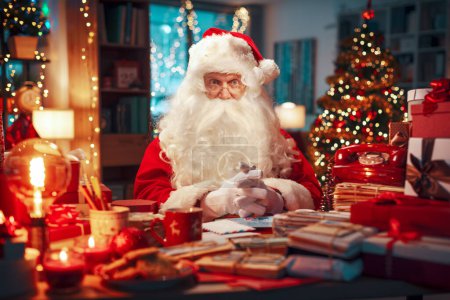 Foto de Feliz Santa Claus sentado en su escritorio y sonriendo a la cámara, Navidad y vacaciones concepto - Imagen libre de derechos