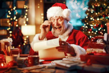 Foto de Feliz Papá Noel alegre sentado en su escritorio y leyendo cartas, Navidad y vacaciones concepto - Imagen libre de derechos