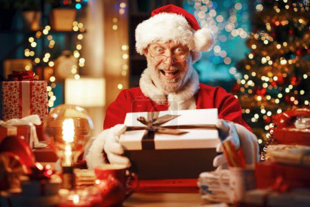 Photo for Happy Santa Claus sitting at his desk and preparing gifts for Christmas - Royalty Free Image