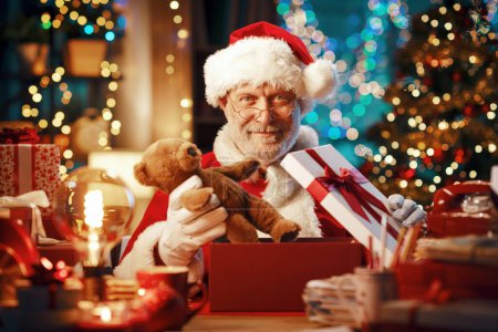Téléchargez les photos : Joyeux Père Noël assis à son bureau et préparant des cadeaux pour Noël - en image libre de droit