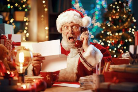 Photo for Angry disappointed Santa Claus holding an expensive invoice and shouting on the phone - Royalty Free Image