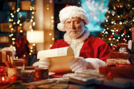 Foto de Pensativo decepcionado Santa Claus sentado en su escritorio y leer cartas, Navidad y vacaciones concepto - Imagen libre de derechos
