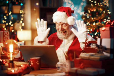 Foto de Feliz Santa Claus teniendo una videollamada con su portátil, está saludando a la pantalla de la computadora y deseando una Feliz Navidad - Imagen libre de derechos