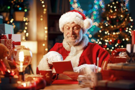Foto de Feliz Santa Claus sentado en su escritorio en casa y conectándose con una tableta digital, Navidad y concepto de tecnología - Imagen libre de derechos