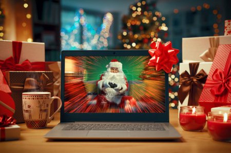 Téléchargez les photos : Joyeux Père Noël tenant une manette de jeu et jouant à des jeux vidéo sur un écran d'ordinateur portable, vacances et concept de divertissement - en image libre de droit