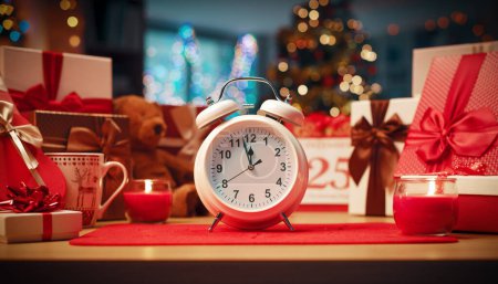 Foto de Reloj despertador de dos campanas que muestra la hora y el interior del hogar decorado para las vacaciones: es Nochebuena - Imagen libre de derechos