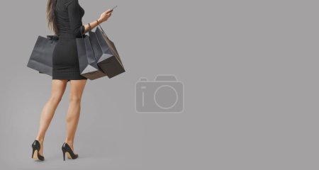 Téléchargez les photos : Belle femme tenant Black Friday sacs à provisions et smartphone, vue arrière, espace de copie - en image libre de droit