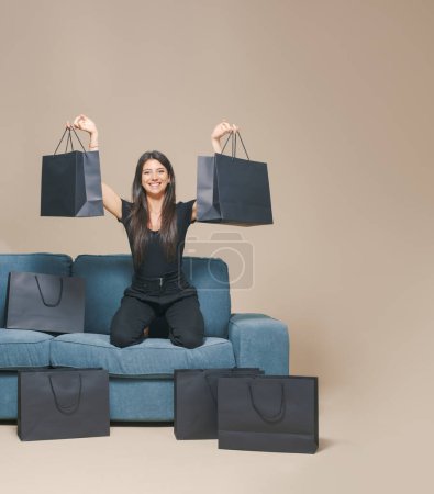 Foto de Mujer feliz sentada en un sofá rodeado de bolsas negras: venta Viernes Negro - Imagen libre de derechos