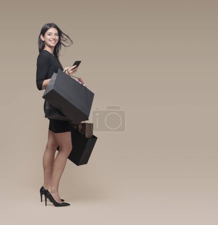 Téléchargez les photos : Jeune femme à la mode tenant des sacs à provisions noirs et un smartphone, elle fait du shopping le vendredi noir - en image libre de droit