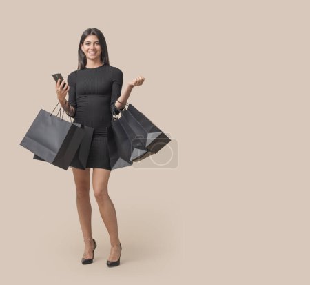 Foto de Feliz mujer de moda sosteniendo muchas bolsas de la compra y un teléfono inteligente, Viernes Negro concepto de venta - Imagen libre de derechos