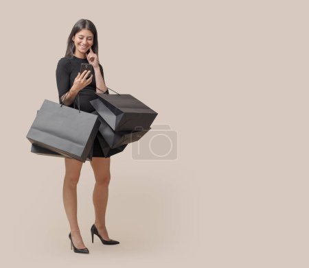 Foto de Hermosa mujer elegante sosteniendo bolsas de compras y haciendo compras en línea en su teléfono inteligente, Viernes Negro venta - Imagen libre de derechos