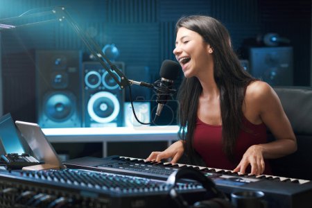 Photo for Young female artist singing and playing the keyboard in the recording studio, creativity and entertainment concept - Royalty Free Image