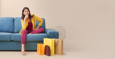 Photo for Happy woman sitting on the couch at home and many shopping bags, sales and shopping concept - Royalty Free Image