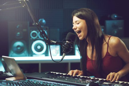 Photo for Young female artist singing and playing the keyboard in the recording studio, creativity and entertainment concept - Royalty Free Image