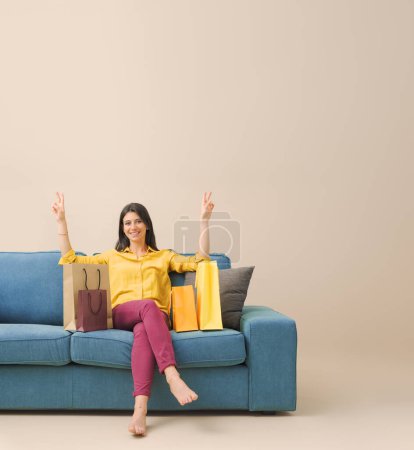 Photo for Happy cheerful young woman sitting on the couch at home and many shopping bags - Royalty Free Image