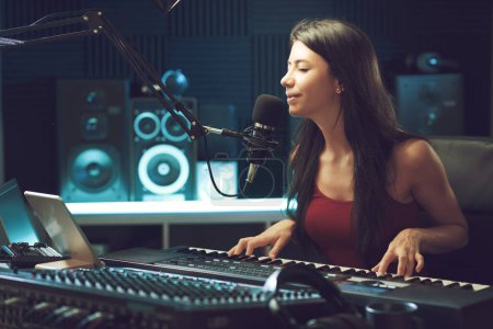 Foto de Joven artista femenina cantando y tocando el teclado en el estudio de grabación, creatividad y concepto de entretenimiento - Imagen libre de derechos