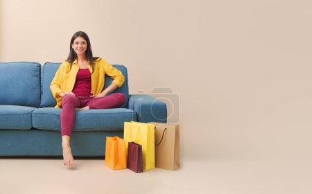 Téléchargez les photos : Femme heureuse assise sur le canapé à la maison et de nombreux sacs à provisions, vente et concept de shopping - en image libre de droit