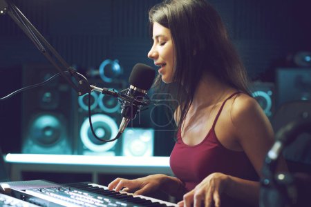 Téléchargez les photos : Jeune artiste féminine chantant et jouant du clavier dans le studio d'enregistrement, concept de créativité et de divertissement - en image libre de droit