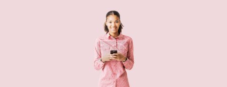 Photo for Smiling young woman standing and using a smartphone - Royalty Free Image