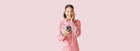 Téléchargez les photos : Jeune femme mignonne utilisant un smartphone, elle est surprise et souriante à la caméra - en image libre de droit
