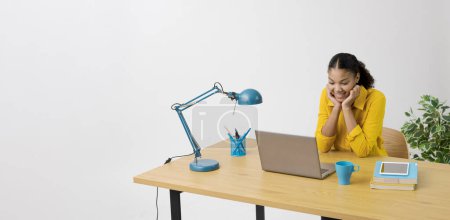 Téléchargez les photos : Femme heureuse assise au bureau et regardant des vidéos en ligne sur son ordinateur portable - en image libre de droit